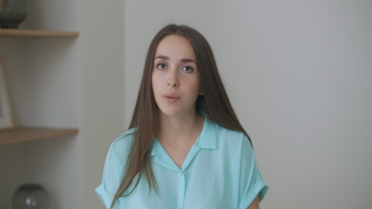 Head shot woman sit on couch look at camera greeting friend start video call. Young adult female with short curly hairstyle enjoy pleasant conversation by video conference event concept