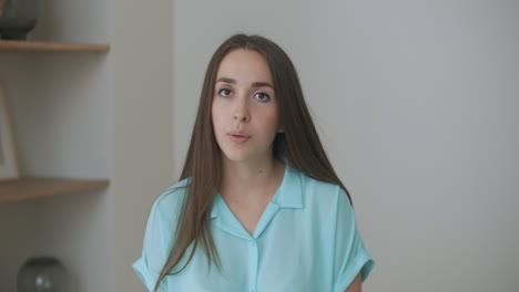 Head-shot-woman-sit-on-couch-look-at-camera-greeting-friend-start-video-call.-Young-adult-female-with-short-curly-hairstyle-enjoy-pleasant-conversation-by-video-conference-event-concept