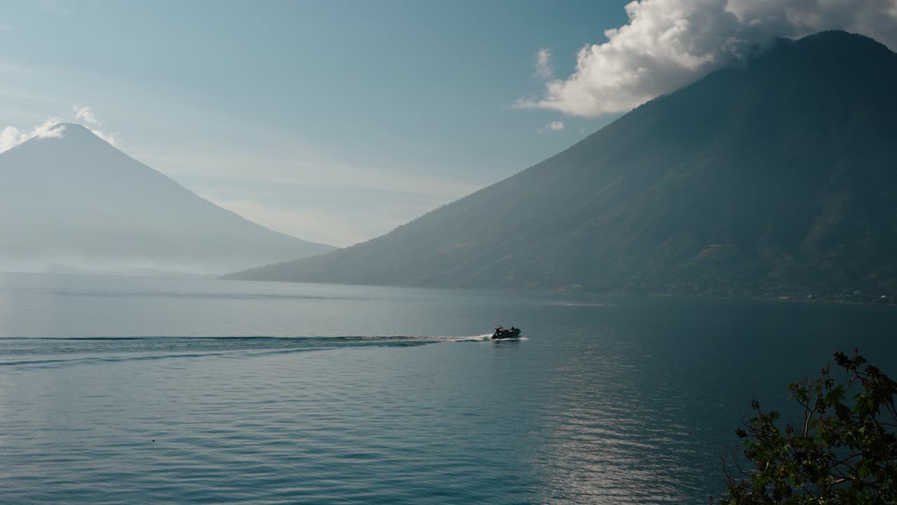 Motorbåd krydser Atitlan-søen med tågede vulkanske tinder i baggrunden