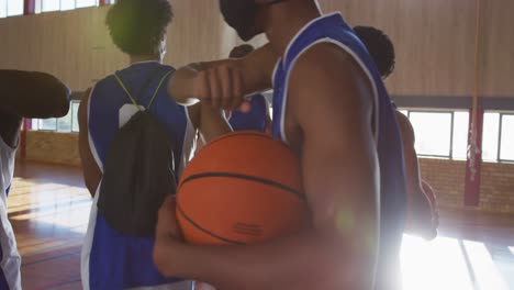 diverse male basketball team wearing face masks and greeting with elbows