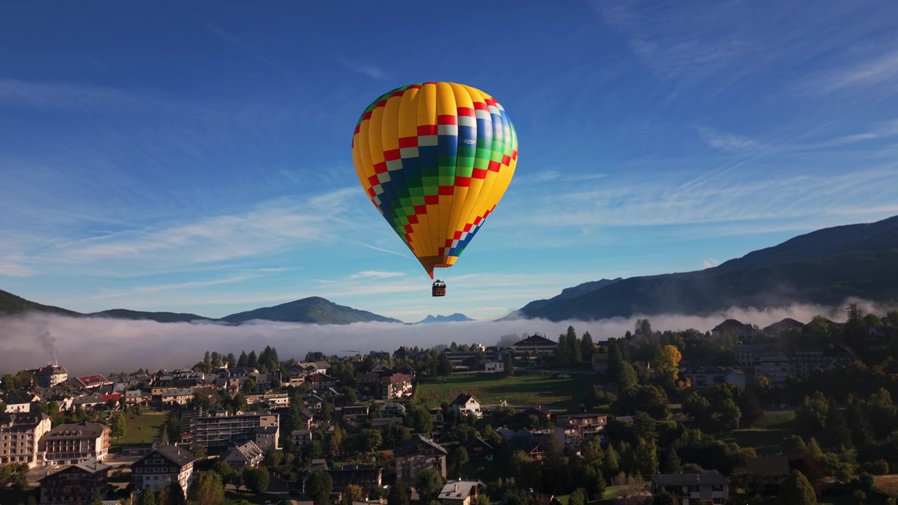 Vista aérea de um balão de ar quente colorido voando sobre uma cidade cercada por neblina em um vale na região de Auvergne-Rhône-Alpes, na França.