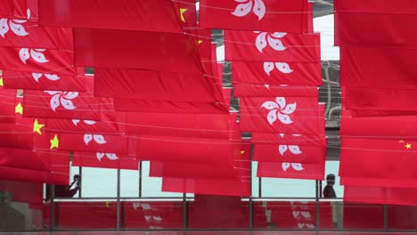 commuters walk through a pedestrian bridge as flags of the people's republic of china and the hong kong sar are seen in a street during hong kong's handover to china anniversary