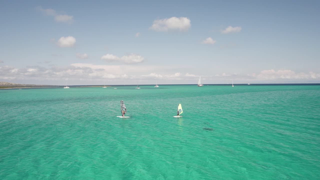 dos windsurfistas se deslizan a través de aguas claras de color turquesa bajo un cielo soleado, toma aérea