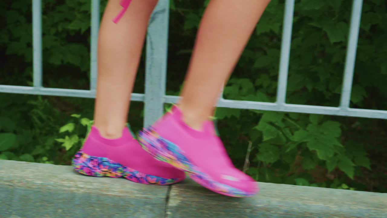 Vibrant Pink Sneakers in Motion: A Close-Up View of Stylish Footwear Walking Along a Pathway Surrounded by Lush Greenery and Secure Railings