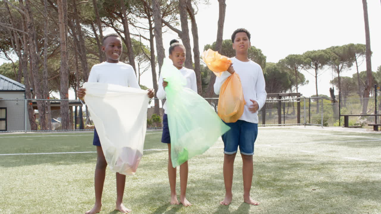 Multiracial students holding colorful bags, cleaning up park, smiling and enjoying teamwork