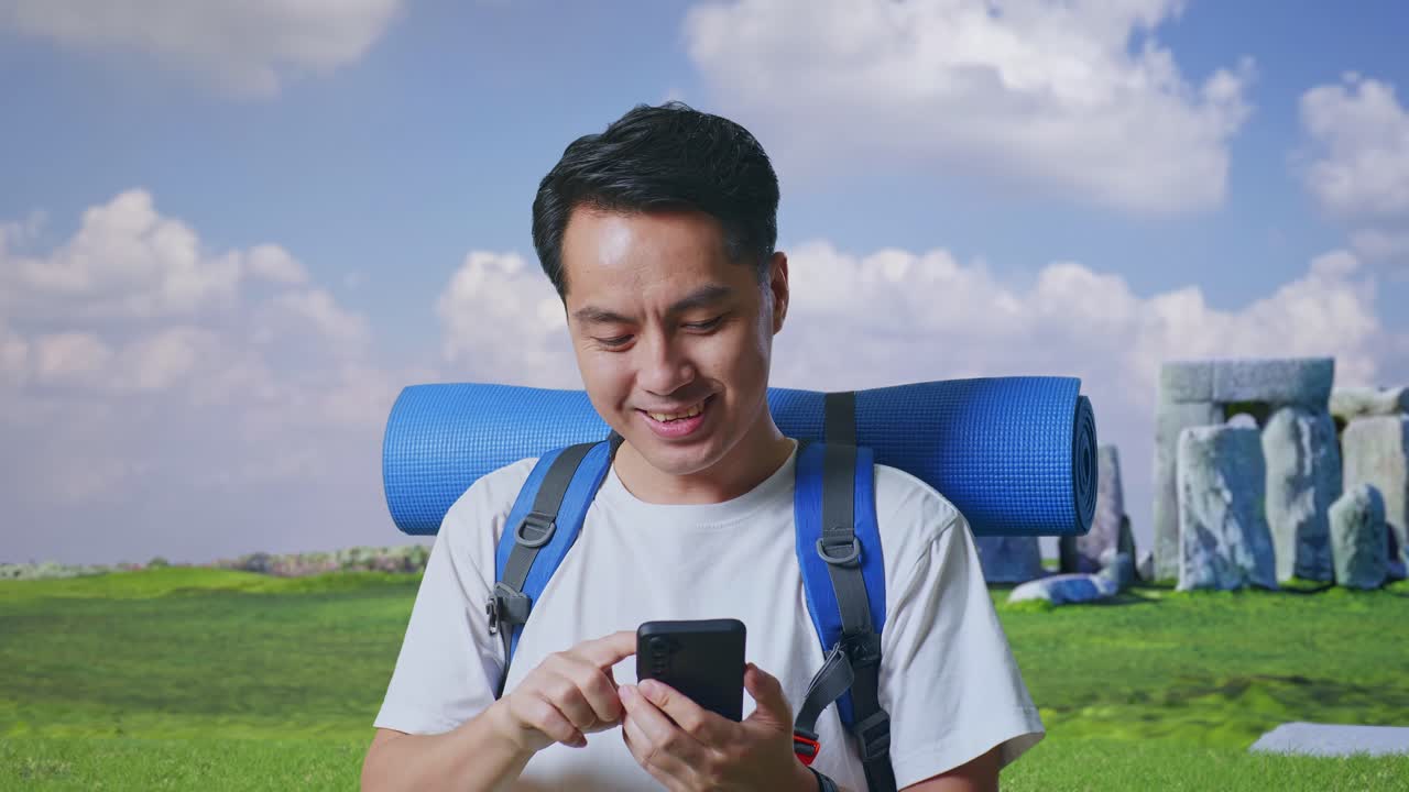 Close Up Of Asian Male Hiker With Mountaineering Backpack Enjoy Using Smartphone While Traveling In Stonehenge