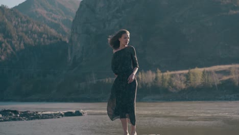 graceful woman stands on rock at river against mountains