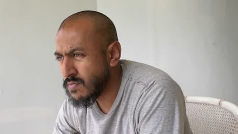 view of asian bangladeshi male sat down looking outward thinking with white wall background