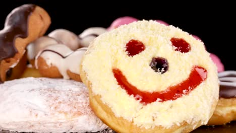A colorful assortment of donuts, including chocolate, pink-glazed, and smiley face varieties, slowly rotates on a glossy black background under bright studio lighting