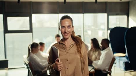 confiada chica feliz en ropa de oficina de negocios sosteniendo una tableta en sus manos, sonriendo y mirando a la cámara en la oficina