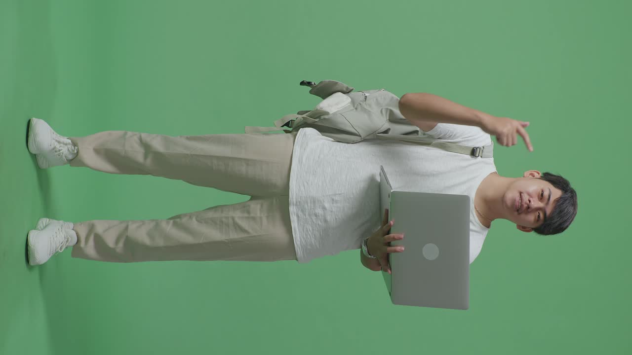 cuerpo lleno de hombre asiático estudiante dedos directos a la computadora portátil en pantalla verde estudio