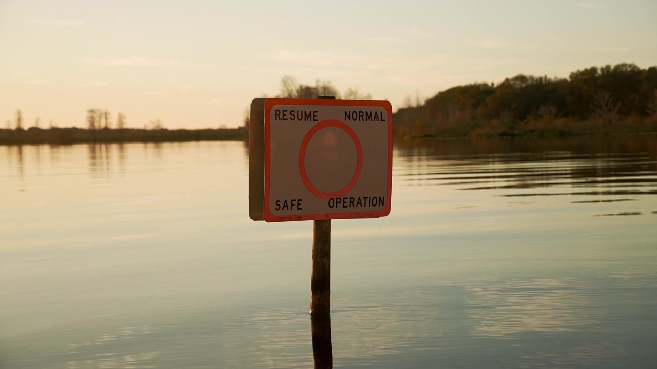 Primo piano di un segnale nautico "Riprendere la normale operazione sicura" che si erge nelle acque a specchio del Lago Minneola a Clermont, Florida, all'ora d'oro