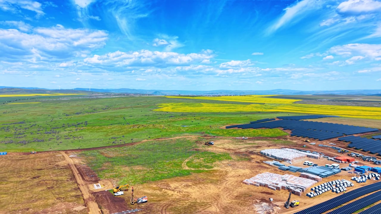 Vue aérienne de la construction d'une ferme solaire à côté de champs verts. Prise de vue en plongée d'un site d'installation de ferme solaire avec des matériaux et des panneaux à côté de champs verts et jaunes.