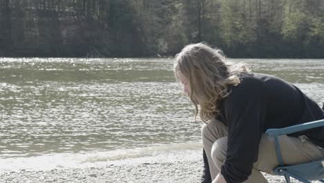 joven de pelo largo sentado junto al río danubio con el hermoso agua brillante en el fondo