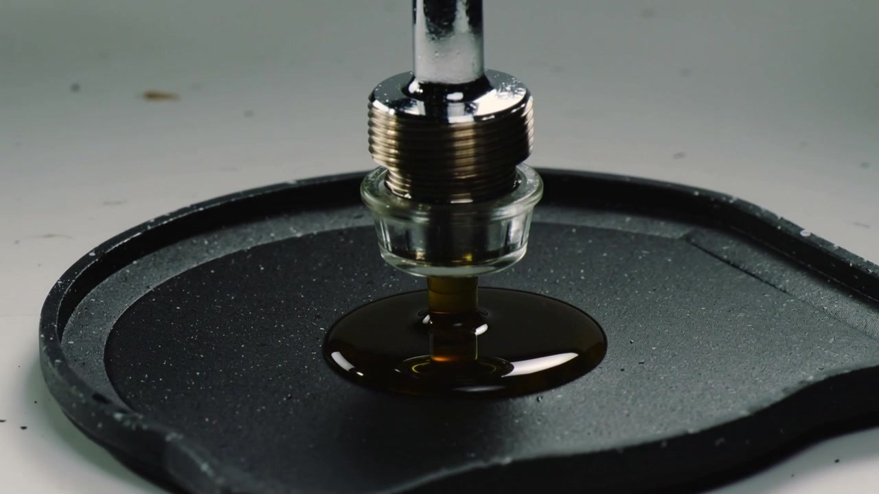 Apertura della valvola, ugello metallico che deposita liquido viscoso color ambra su un cuscinetto di gomma per il test.