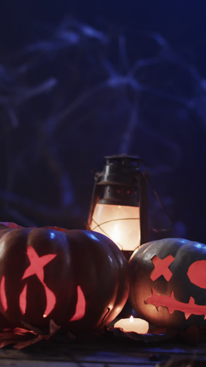 Vertical video of halloween carved pumpkins, candle and smoke with copy space on blue background