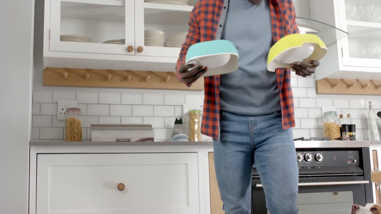 African american man giving food to his pet dogs in kitchen at home, slow motion