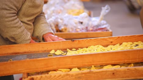 ancianas haciendo y secando pasta orecchiette tradicional hecha a mano, cuidando y atendiendo a los estantes mientras habla con el cliente, brillantes y cálidos, estantes de madera de pasta amarilla, tiro estático sin rostros