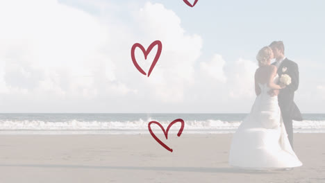 animation of red hearts over caucasian couple wearing wedding clothes and kissing on beach