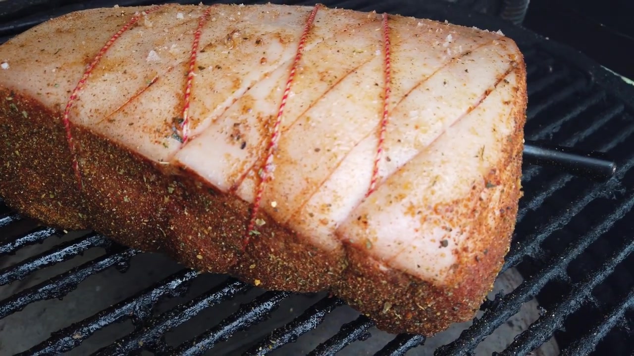 Délicieux rôti de filet de porc assaisonné, ficelé avec de la ficelle de boucher, fumant sur un barbecue chaud. Cuisson en extérieur d'un plat de viande gastronomique.