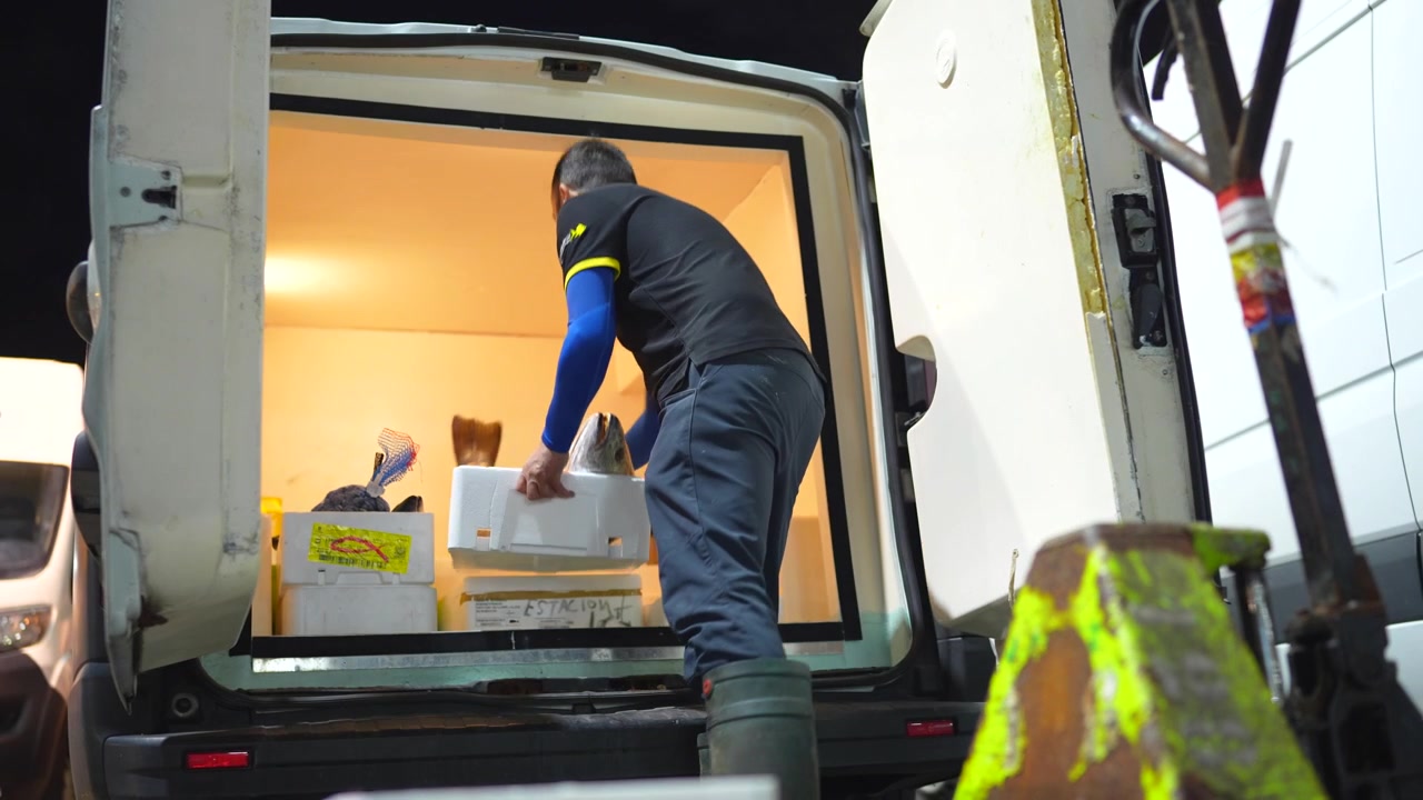 Male worker loading styrofoam boxes of freshly caught fish into a refrigerated delivery vehicle