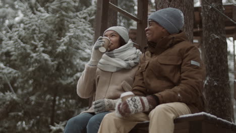 couple enjoying hot drinks in a snowy forest treehouse