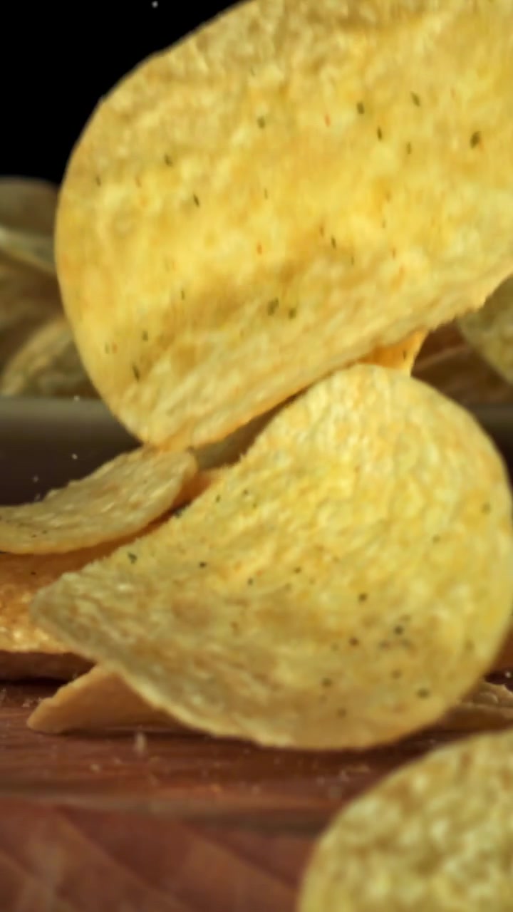 Golden Potato Chips Falling in Slow Motion onto a Wooden Surface