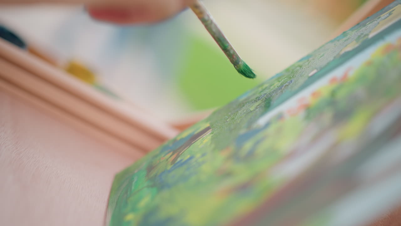 Dettaglio di un artista che dipinge a mano un paesaggio in miniatura con un pennello sottile, pigmenti verde vivido, strati materici, pennellate precise, luce soffusa da studio e un'atmosfera tranquilla che trasmette concentrazione e creatività
