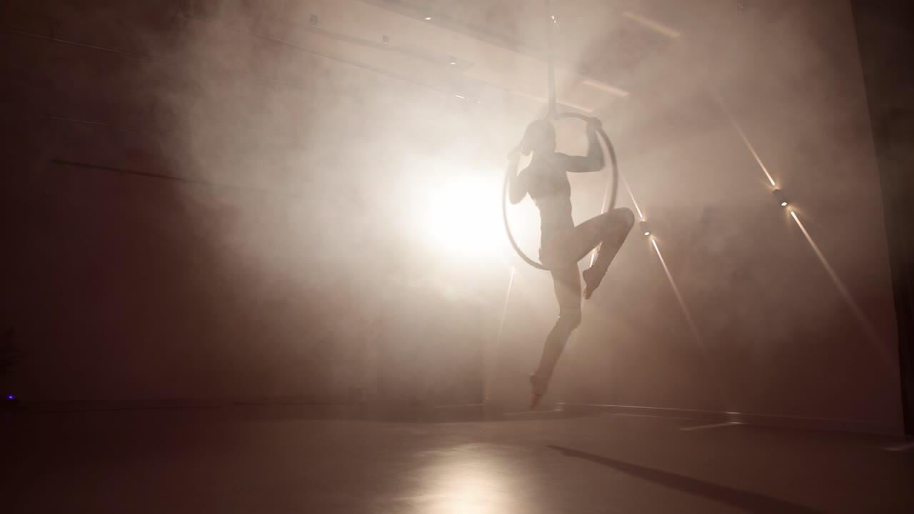 Aerial hoop female dancer performing in a smoky room