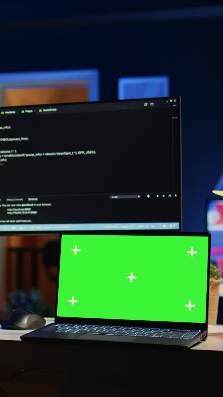 Laptop with Green Screen and Computer Monitor with Code at Night