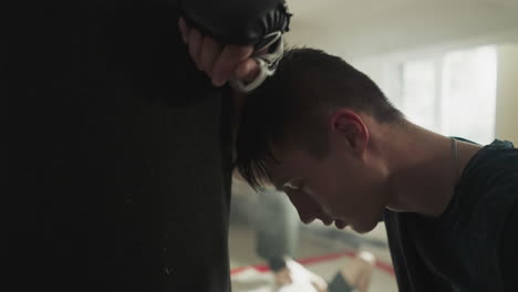 exhausted man leans head on punching bag after intense exercise to improve physical health and endurance at sports club. workout until lose energy and improve muscle mass