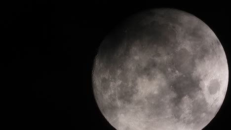 Zoomed-in-big-full-Moon-is-floating-on-black-night-sky,-dramatic-dark-clouds-passing-over---timelapse