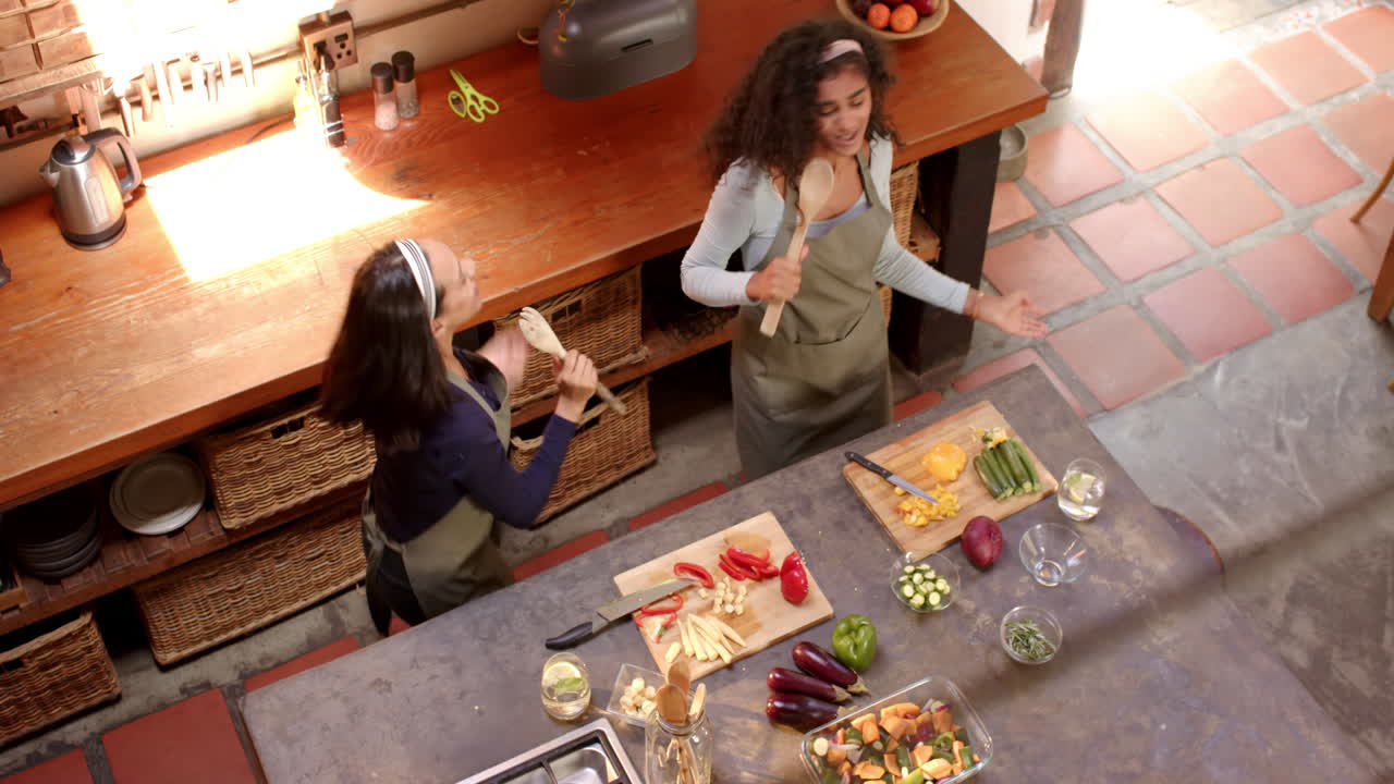 Duas amigas multirraciais preparando alegremente uma refeição juntas em uma cozinha aconchegante, em casa.