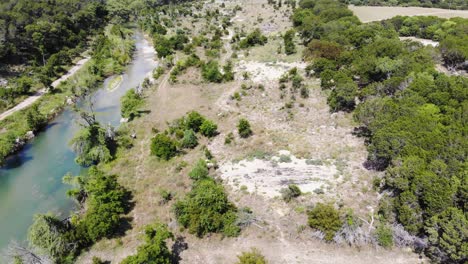 Drone-decent-above-field-with-small-trees,-open-field,-and-sandy-area