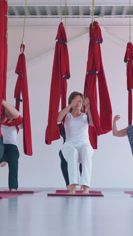 slim women standing in warrior poses move and release legs from special aerial fly yoga red hammocks