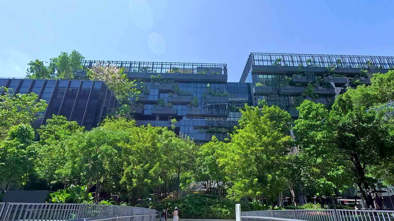 A contemporary building with greenery in Bangkok under clear blue skies, captured with dynamic camera movement