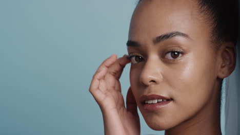 close up portrait attractive african american woman touching face with hand caressing smooth healthy skin complexion enjoying perfect natural beauty on blue background copy space