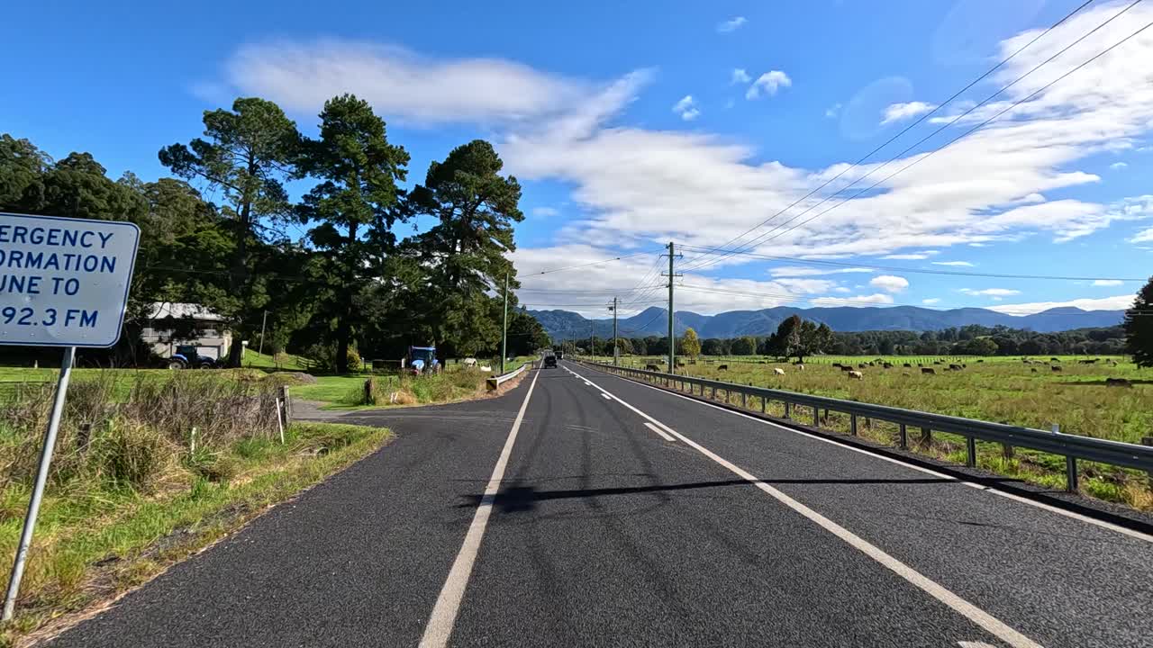 A serene drive along a rural road in Bellingen, Australia, showcasing lush landscapes and clear skies