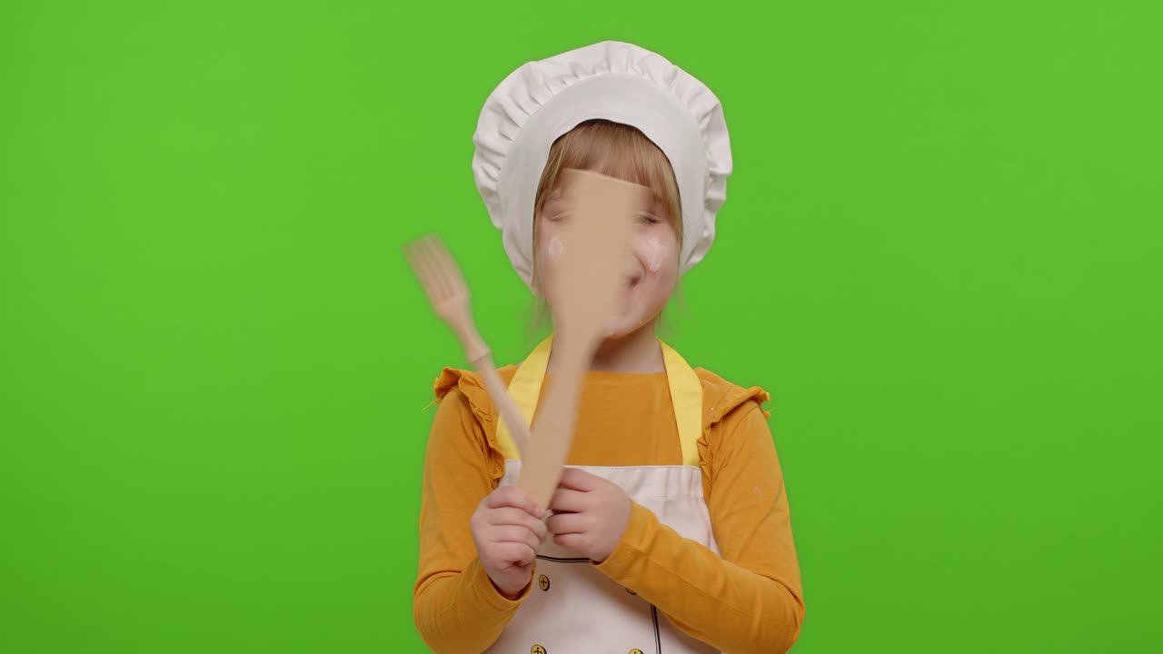 Bambina vestita da cuoca che mostra una forchetta di legno e una spatola, sorridente, che balla su chroma key.