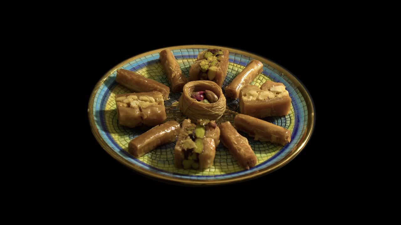 Piatto con bordo dorato di dolce baklava che ruota su sfondo nero.