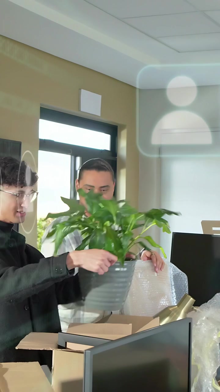 Video vertical: Equipo desempacando, colocando una planta y quitando el envoltorio, mientras una pantalla de guía de RA asiste en la configuración de la oficina.