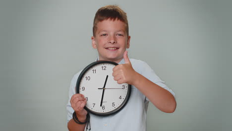 Toddler-kid-boy-showing-time-on-wall-office-clock,-ok,-thumb-up,-approve,-pointing-finger-at-camera