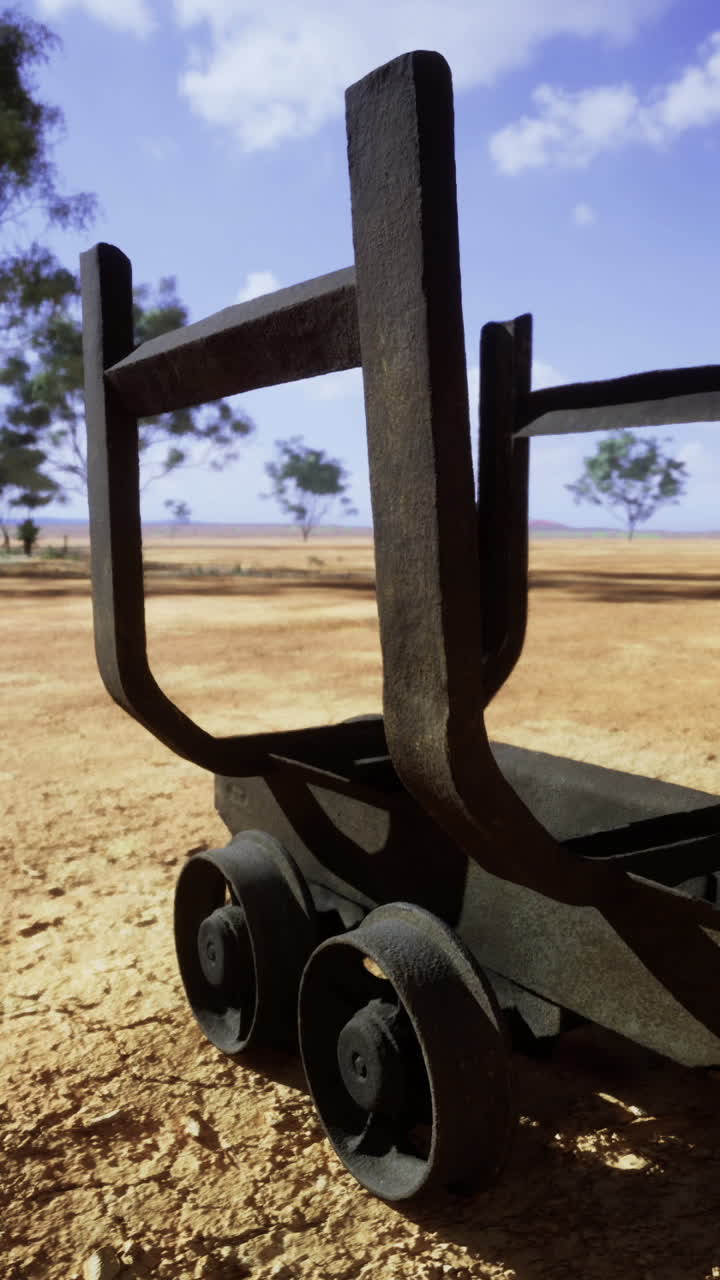 Rusty cart rests under blue skies in a vast arid landscape filled with trees