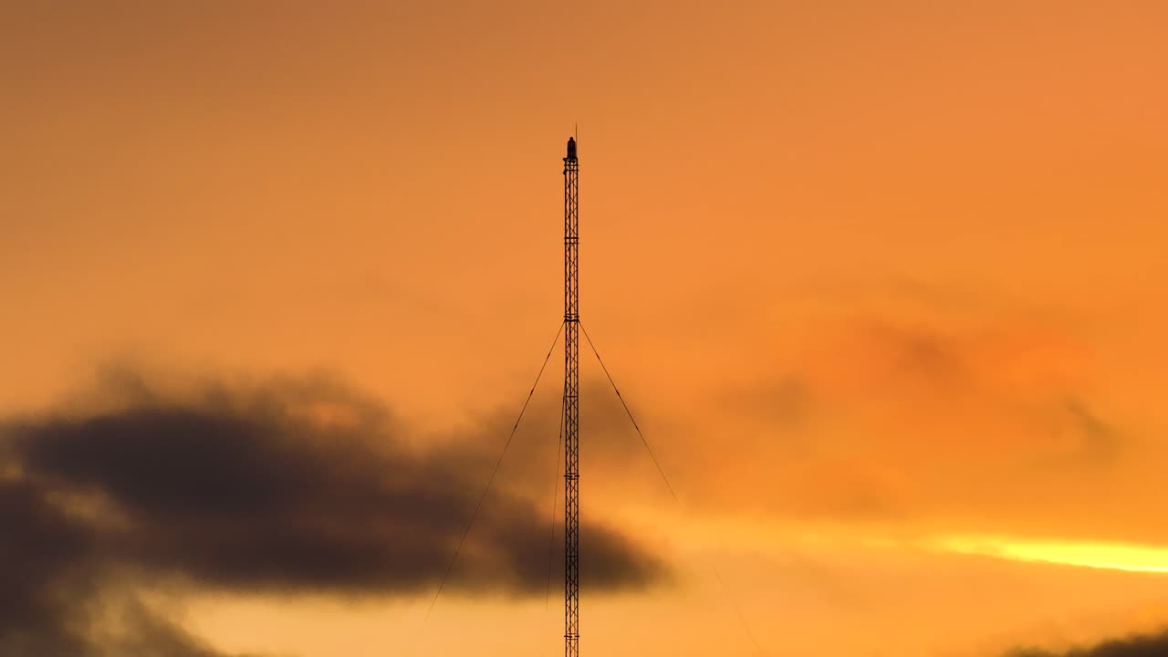 Golden hour orange sunset behind a tall electric radar tower with warm ambient haze, time lapse
