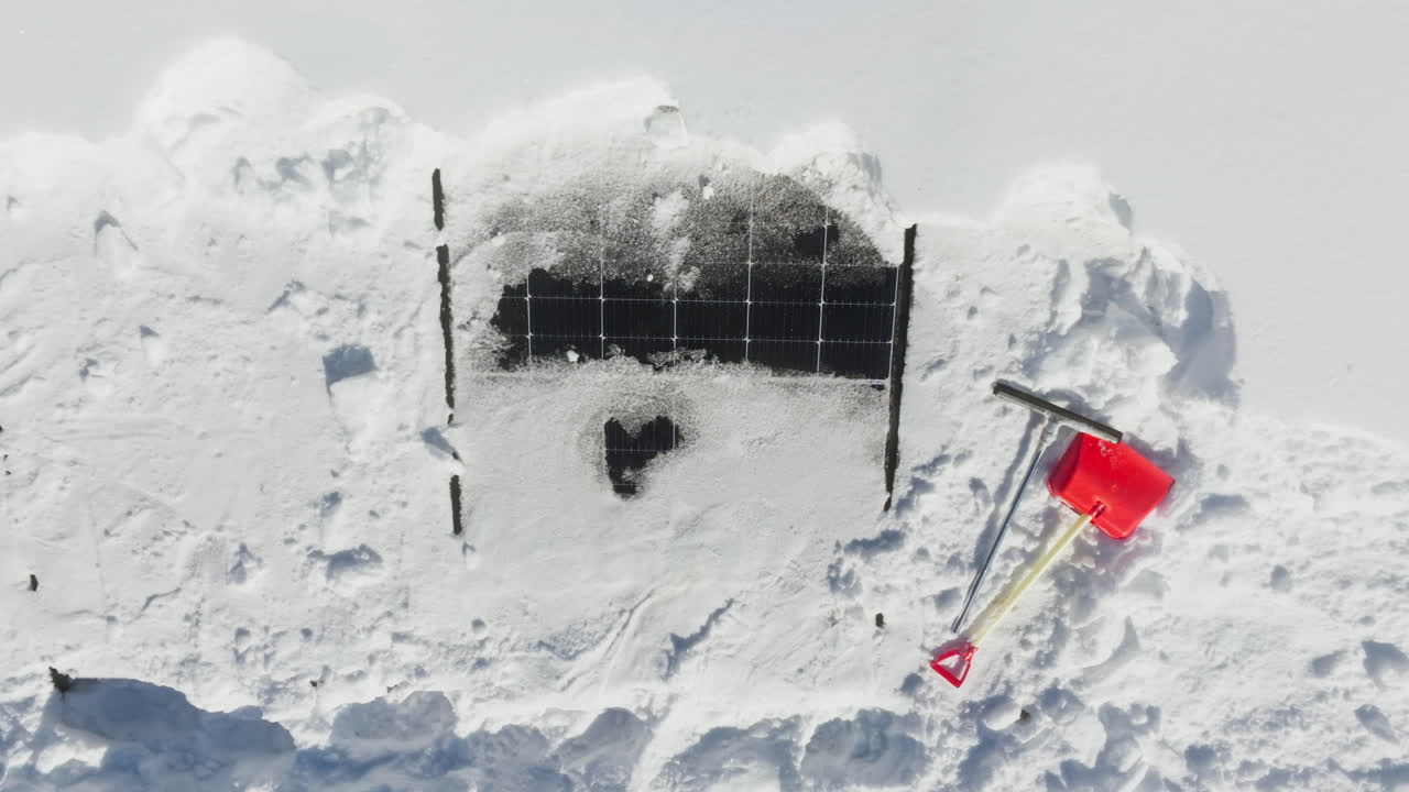 Aerial view of a plastic shovel and a rubber scraper at snowy solar cells on a house roof