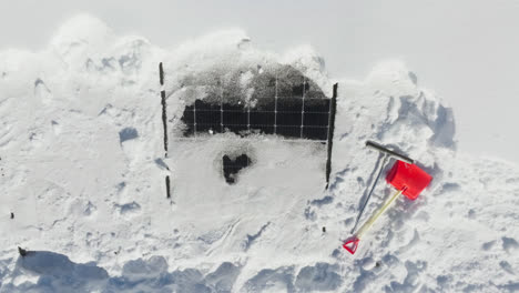 aerial view of a plastic shovel and a rubber scraper at snowy solar cells on a house roof