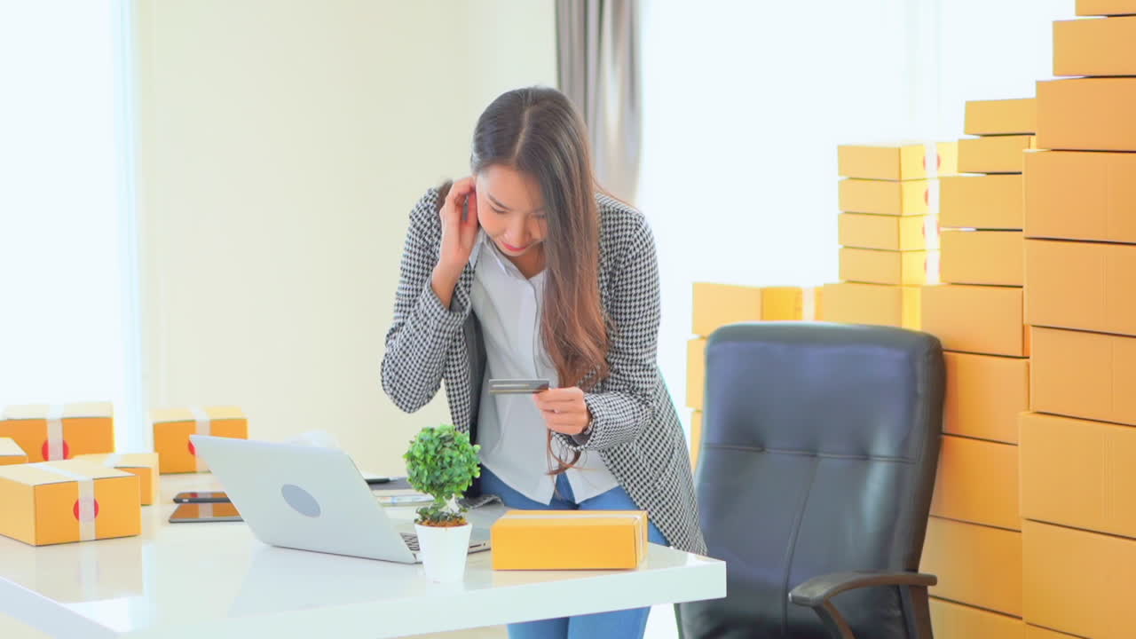 cámara lenta de mujer rodeada de cajas amarillas comprando en línea con tarjeta de crédito y computadora portátil