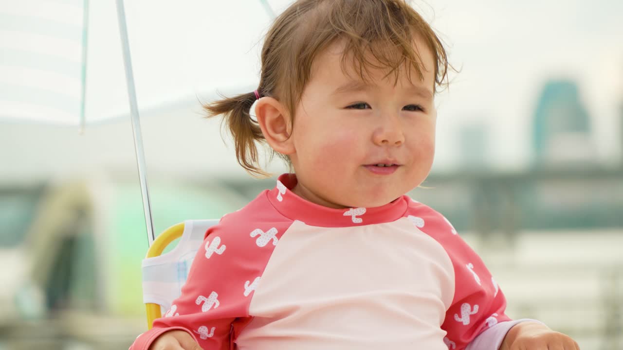 우산 아래 아이의 해변 의자에 앉아 노래를 부르는 행복한 2살 소녀