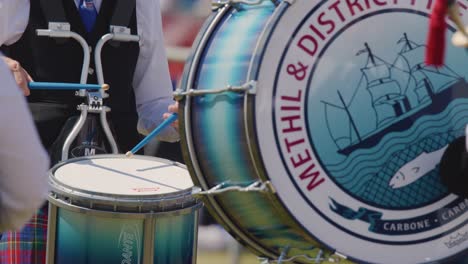 Scottish pipe band drummer in traditional uniform playing snare drum outdoors during daytime event