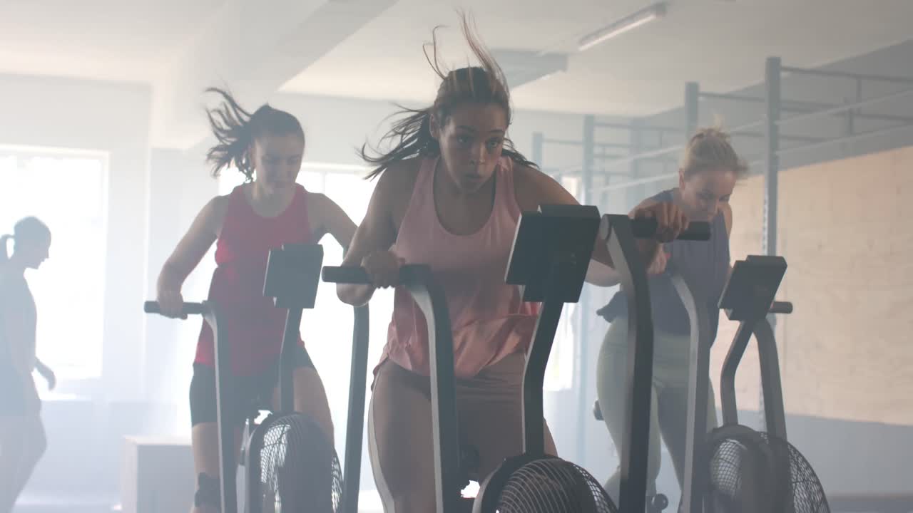 그룹 피트니스 수업에서 타원형 자전거를 타고 훈련하는 다양한 여성, 느린 동작